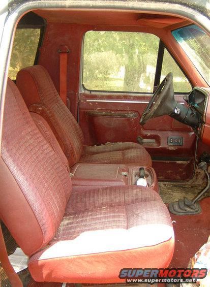 Interior shot of a red SUV, showing front seats, steering wheel, and gear shifter. Looks like a Ford Bronco