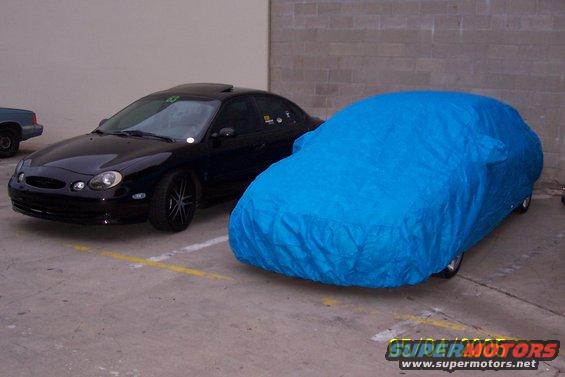 Black sedan parked next to a car covered in a blue tarp. The sedan appears to be a 1998 Mercury Sable