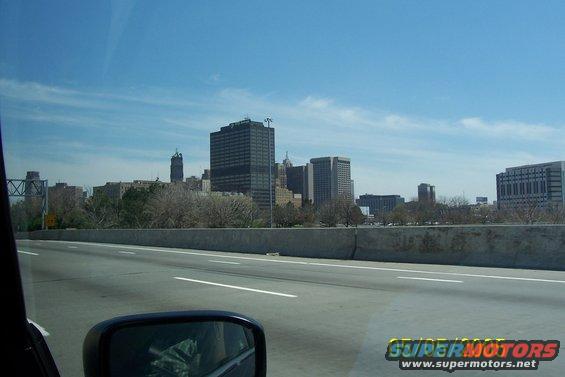 Highway view of city skyline with a concrete barrier and a side mirror reflecting interior