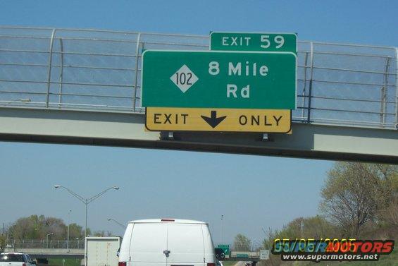 Highway exit sign for 8 Mile Rd, Exit 59, with a white van visible below