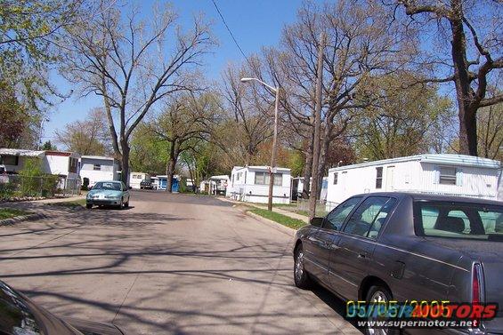 Street in a mobile home park with several trailers and two cars visible