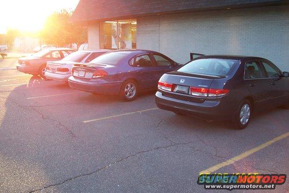 Several sedans parked in a lot at sunset. One is a dark Honda Accord
