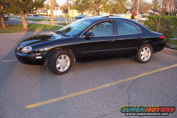 Black 1998 Mercury Sable sedan parked on asphalt with a yellow line. The car is viewed from the front three-quarter angle