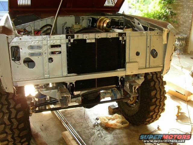 Front of a Ford Bronco with hood open, showing engine bay and radiator. Tires are large and knobby