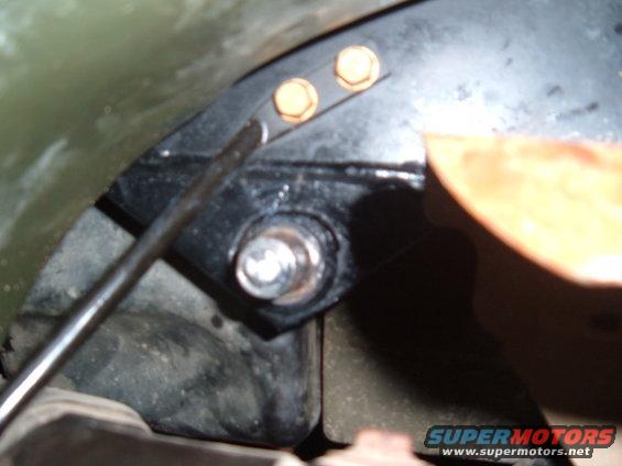 Close-up of a metal bracket with two gold bolts and a silver bolt, attached to a black component. A metal rod is visible