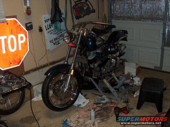 Motorcycle on a lift in a garage with tools on the floor and a stop sign on the wall