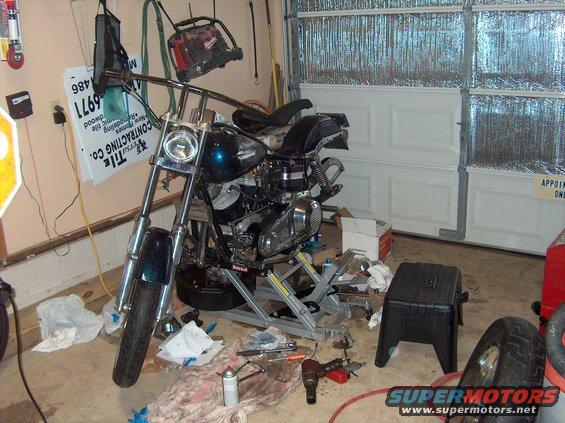 Motorcycle on a lift in a garage, with tools scattered around. It has a teal-colored fuel tank and chrome handlebars