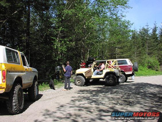 Yellow and white Ford Bronco parked next to a yellow Jeep and a red Ford Bronco in a wooded area