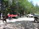 1993 Ford Bronco - Several off-road vehicles and people are gathered in a wooded area, with a red trailer being moved.