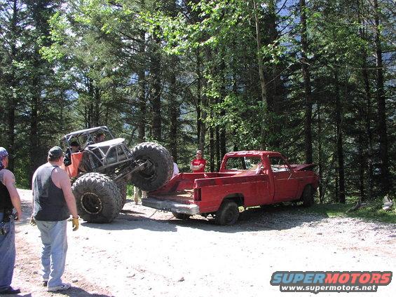 Red pickup truck with an orange off-road vehicle being loaded onto its bed, outdoors with trees