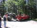 1993 Ford Bronco - An off-road vehicle is loaded onto the bed of a red pickup truck in a wooded area.