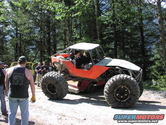 Orange custom buggy with large tires and roll cage, parked on dirt road