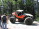 1993 Ford Bronco - A custom-built off-road buggy with oversized tires and a prominent roll cage is seen on a dirt path, with other vehicles and people in the…