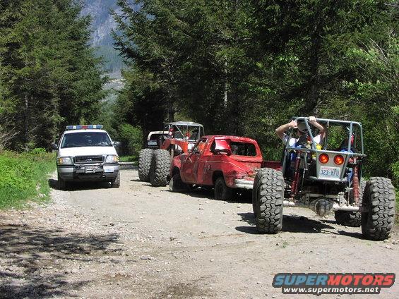 White SUV, red pickup truck, and off-road buggy on a dirt road