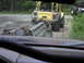 1993 Ford Bronco - A yellow Jeep Wrangler tows a heavily damaged vehicle on a gravel road, with another Jeep in the distance.
