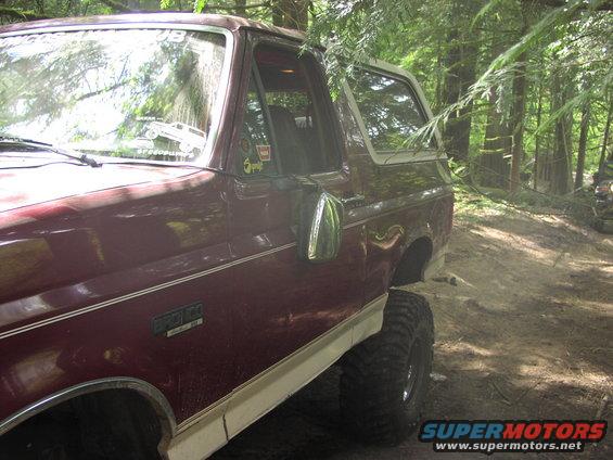 Maroon 1993 Ford Bronco with white top, seen from the side in a forest