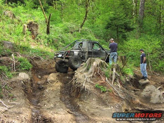 Off-road vehicle with a roll cage on a steep, muddy trail with two people watching