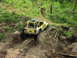 1993 Ford Bronco - A yellow off-road jeep navigates a steep, muddy track with a dog observing from the side.