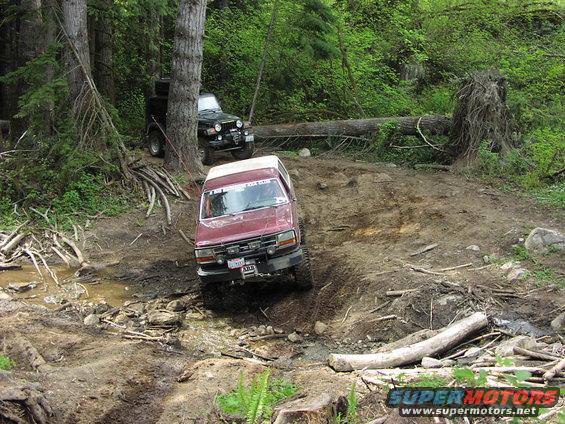 Red SUV navigating muddy off-road terrain with a Jeep in the background