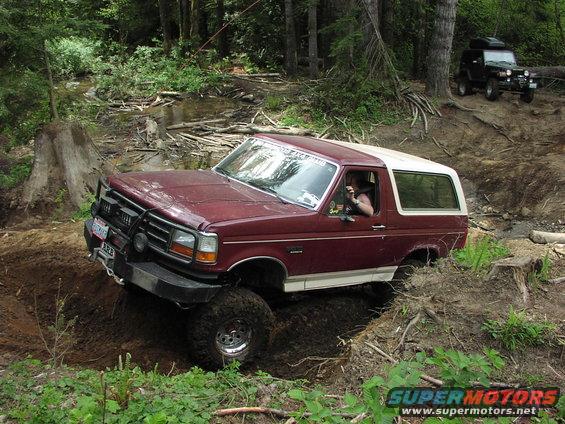 1993 Ford Bronco navigating a muddy off-road trail with another SUV in the background