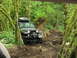 1993 Ford Bronco - A black Jeep Wrangler navigates a challenging, muddy trail through a moss-covered forest.