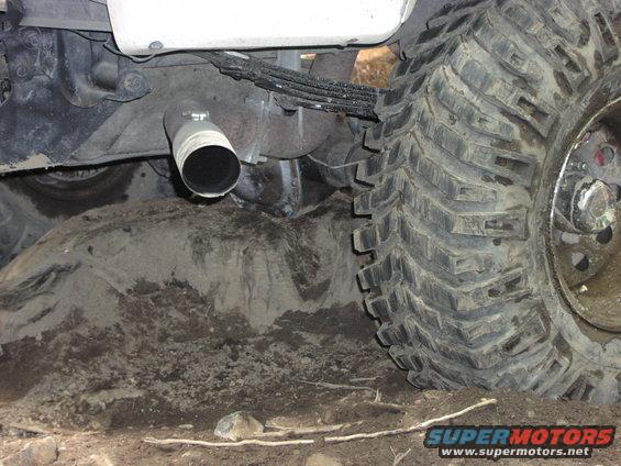 Close-up of a large off-road tire and exhaust pipe stuck in dirt