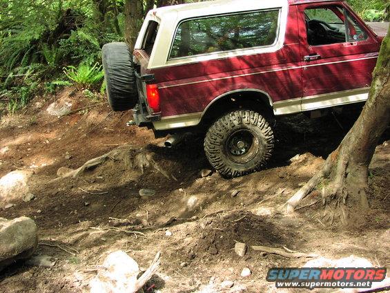 Maroon and white Ford Bronco on a dirt trail, with a spare tire mounted on the rear