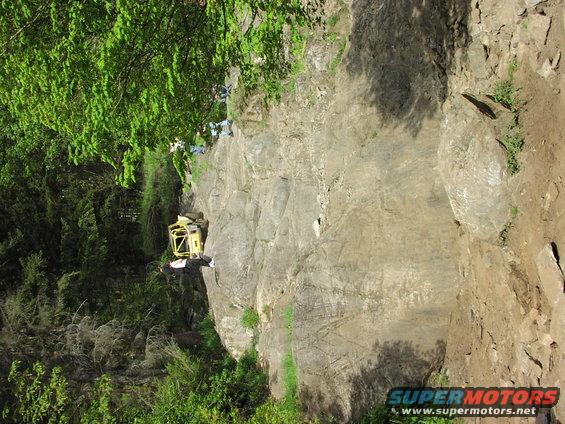 yellow off-road vehicle with roll cage on a steep, rocky incline near trees