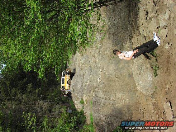 Yellow off-road vehicle navigating a steep, rocky trail with a person watching from above