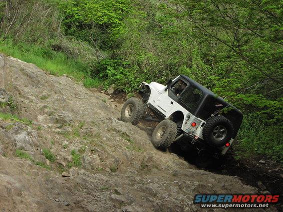 White Jeep Wrangler with large tires climbing a steep, rocky incline. Black hardtop