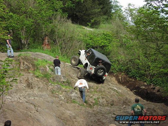 White Jeep Wrangler tilted on a rocky incline with a black soft top