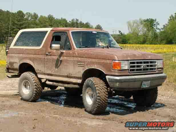 Brown 1987 Ford Bronco with white top on a dirt road