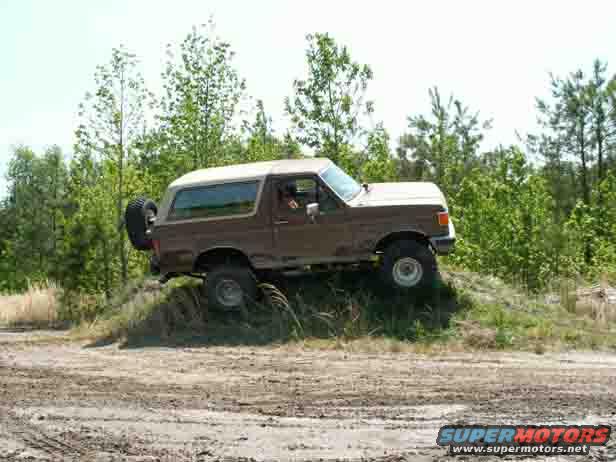 Brown Ford Bronco climbing a dirt hill with trees in the background