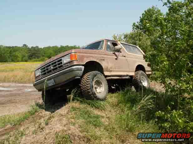 Brown Ford Bronco on grassy incline, front-left tire off the ground