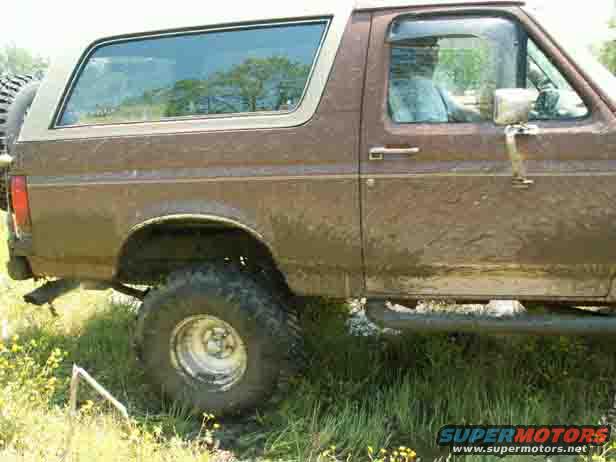 Side view of a brown Ford Bronco with a white top, parked in grass