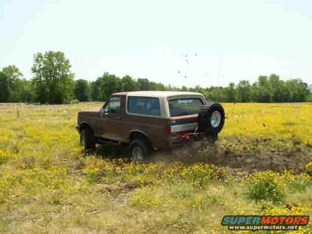 Brown Ford Bronco driving through mud in a field