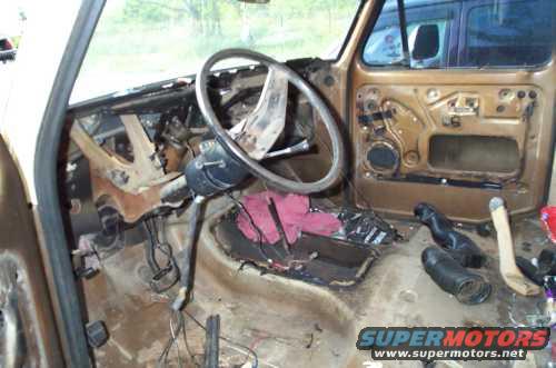 Interior of a vehicle with dashboard removed, showing steering column, door panel, and floor