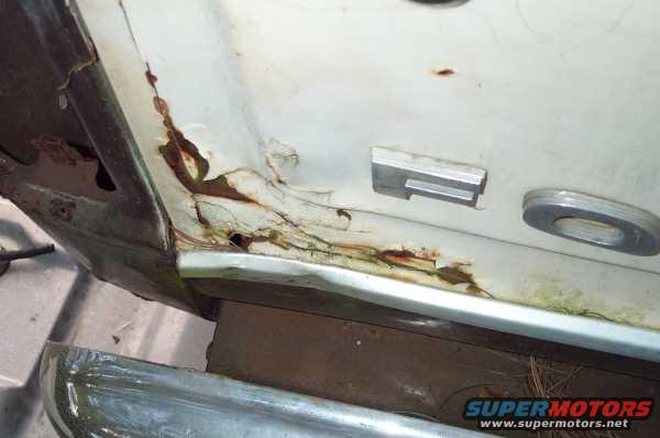 Close-up of a heavily rusted white vehicle door panel showing trim pieces and extensive corrosion