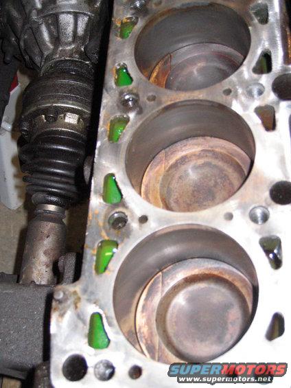 Engine block showing three cylinders with pistons inside. Green liquid is visible in some coolant passages