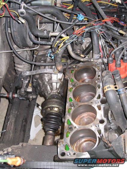 Engine block with cylinders and transmission components, wires and hoses visible