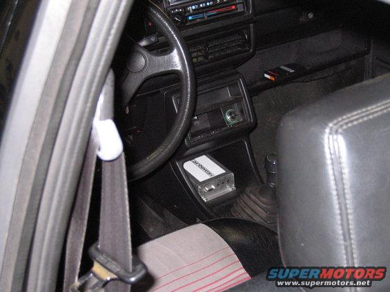 Car interior showing steering wheel, dashboard, gear shifter, and an aftermarket amplifier