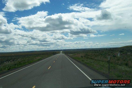 Long empty highway stretching to the horizon under a cloudy blue sky