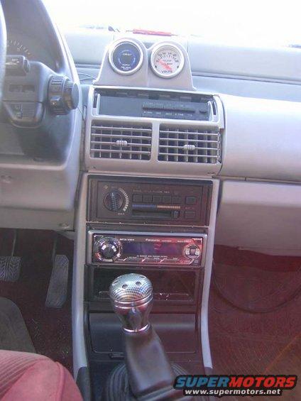 Car interior showing dashboard with two gauges, a stereo, and a manual shifter
