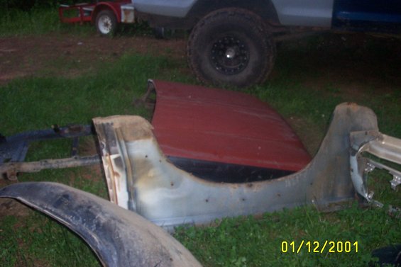 Red hood and fender parts scattered on grass with a trailer and vehicle in the background