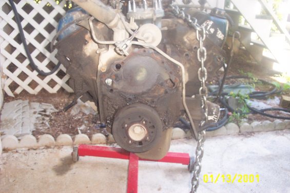 engine block on red stand, covered in grime, with a chain attached