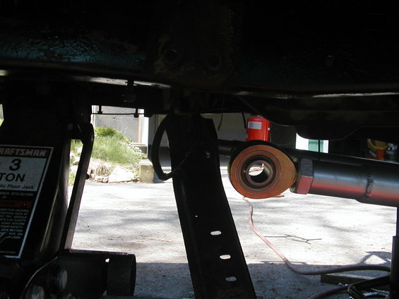 Vehicle frame supported by a Craftsman floor jack, showing suspension components and a red fire extinguisher in the background