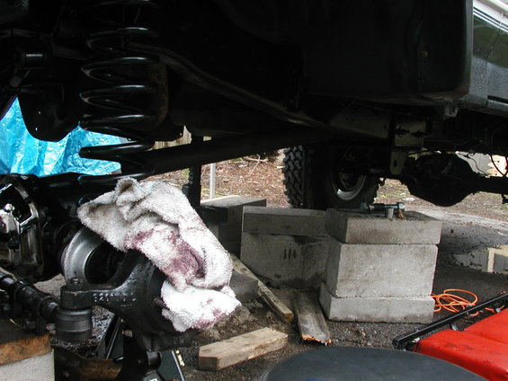 Underside of a vehicle being worked on, with suspension components visible. A dirty rag is on the axle