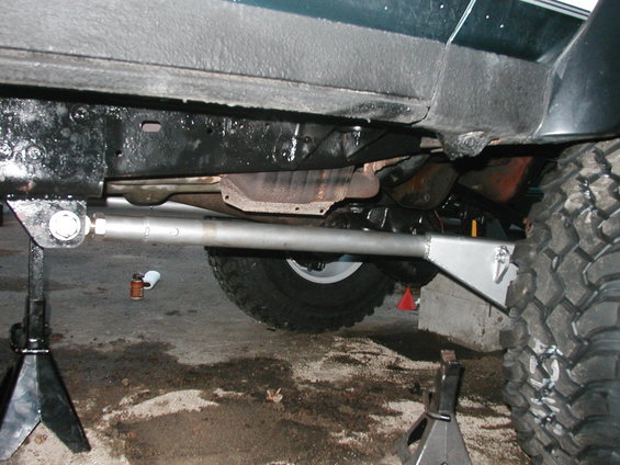 Green vehicle's underside with aftermarket suspension parts and large tires on jack stands