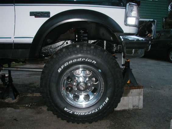 White Ford Bronco with black fender flares and BFGoodrich Mud-Terrain T/A tires on chrome rims, lifted and on jack stands