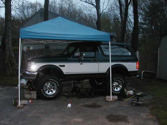 1994 Ford Bronco lifted on jack stands under a blue canopy